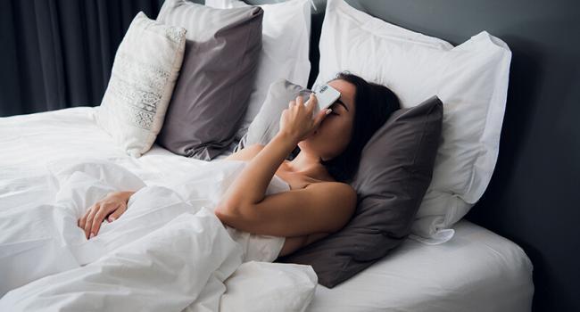 Tired girl sleeping in a bed. Fall asleep with the cell phone on her face. Facepalm gesture with a phone.