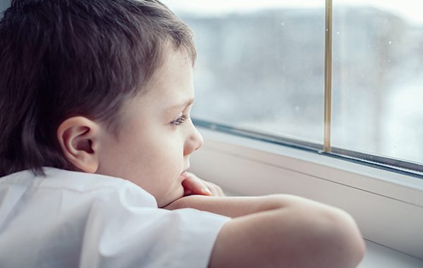 one sad little boy sitting near the window at the day time. Concept of sorrow.