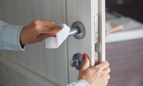 Woman cleaning the door handle with disinfecting wipe