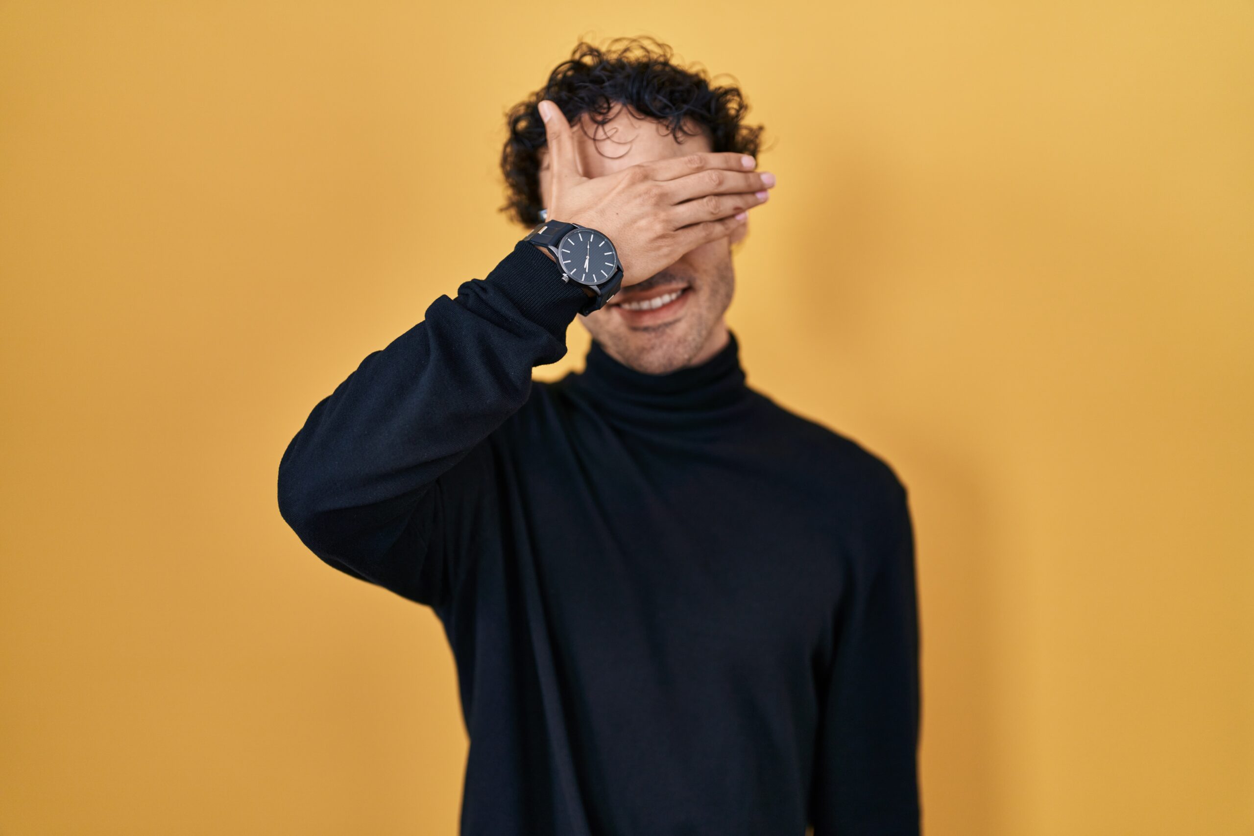 Hispanic man standing over yellow background smiling and laughing with hand on face covering eyes for surprise. blind concept. hipnose para timidez